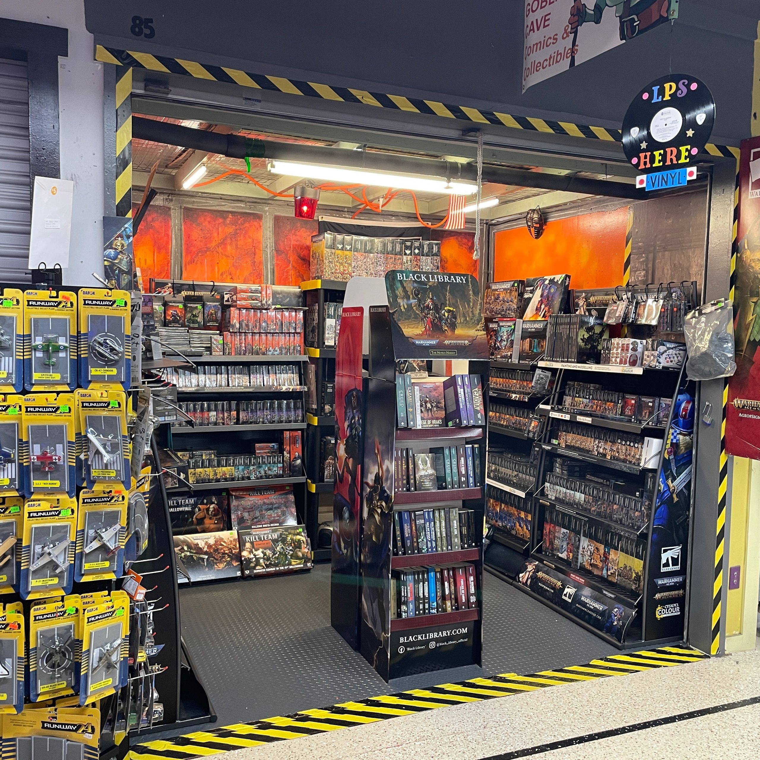 A vibrant comic and collectibles store corner with shelves full of items and a Black Library display