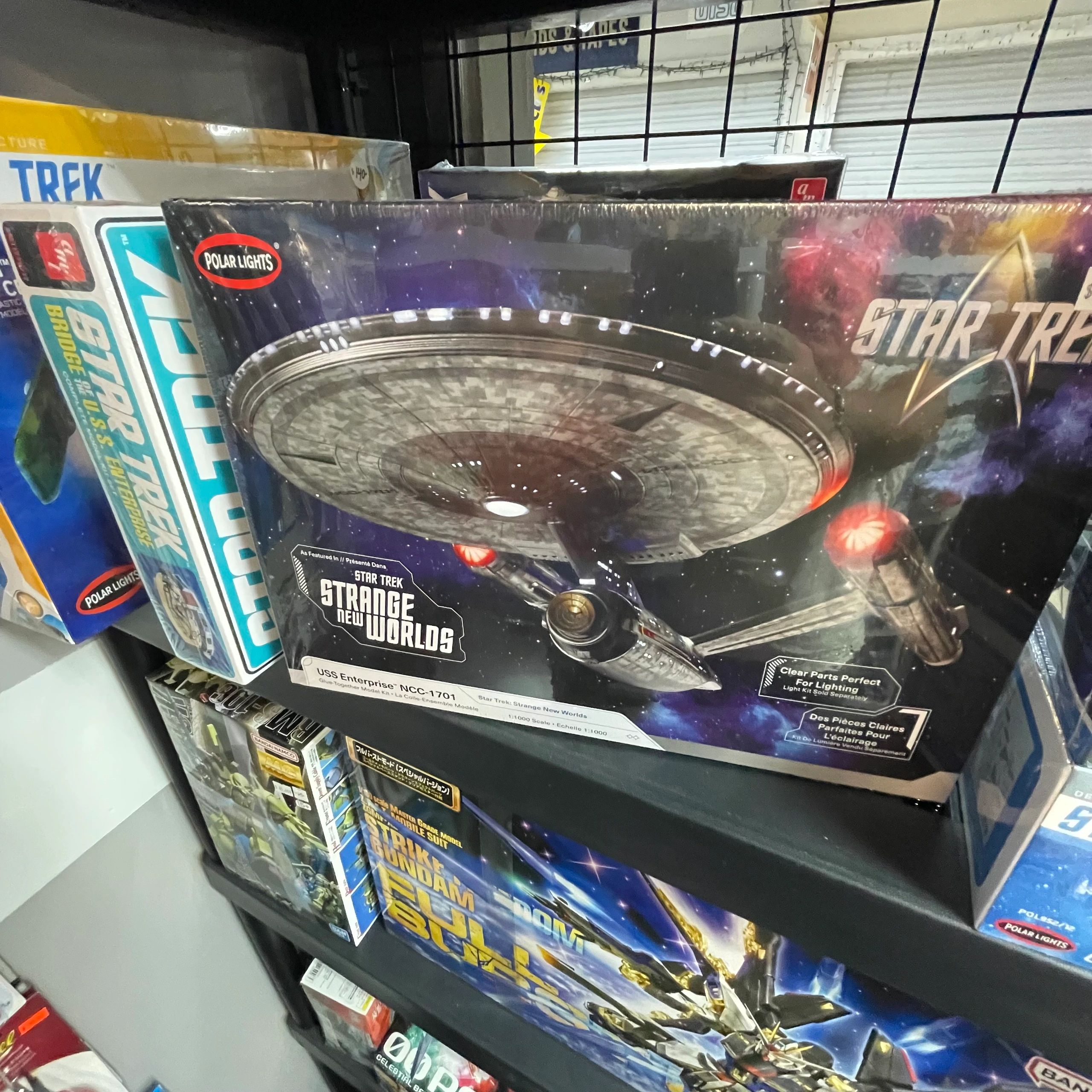 Star Trek model kits displayed on a shelf, featuring the USS Enterprise from Strange New Worlds