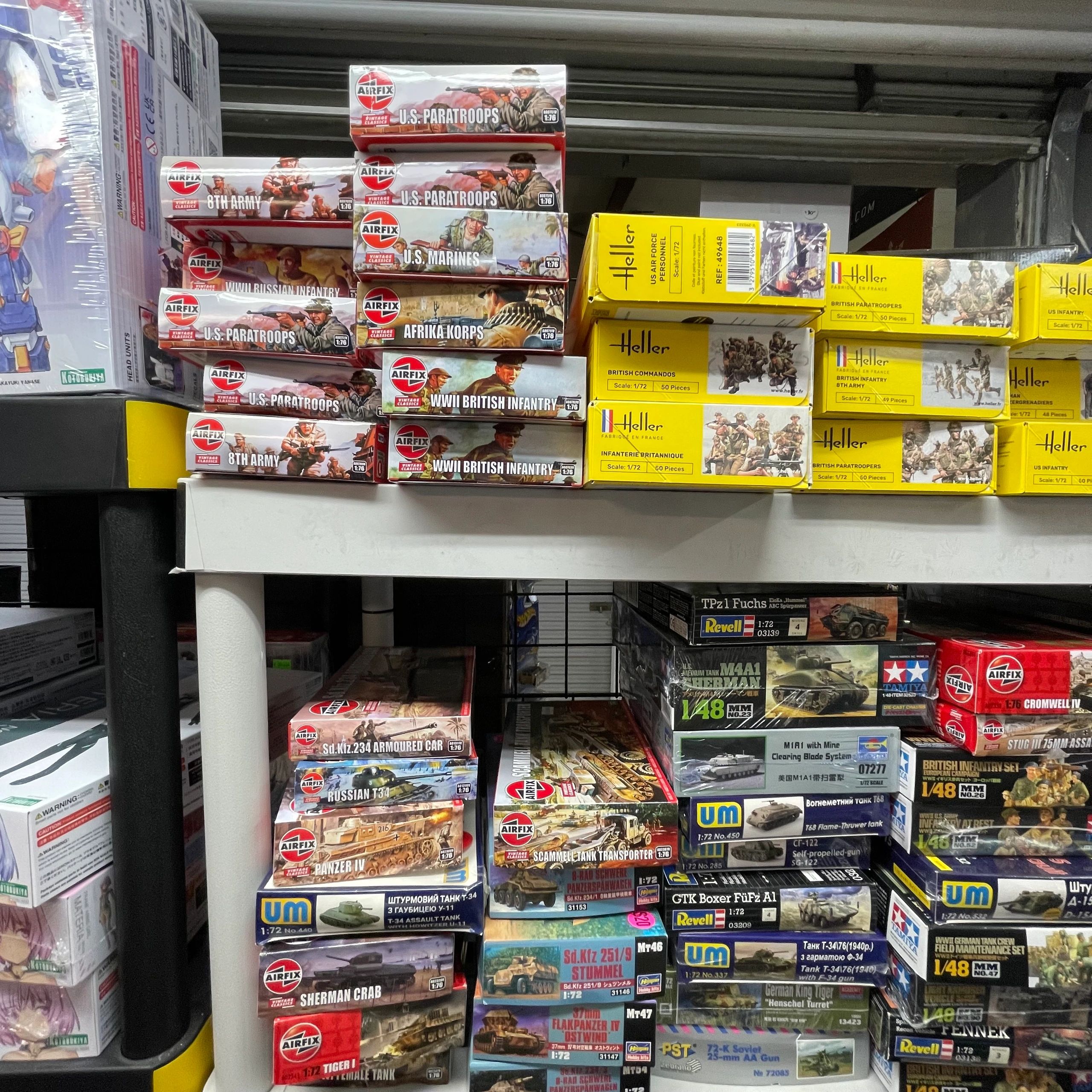 Shelves stocked with various military model kits from brands like Airfix, Heller, and UM