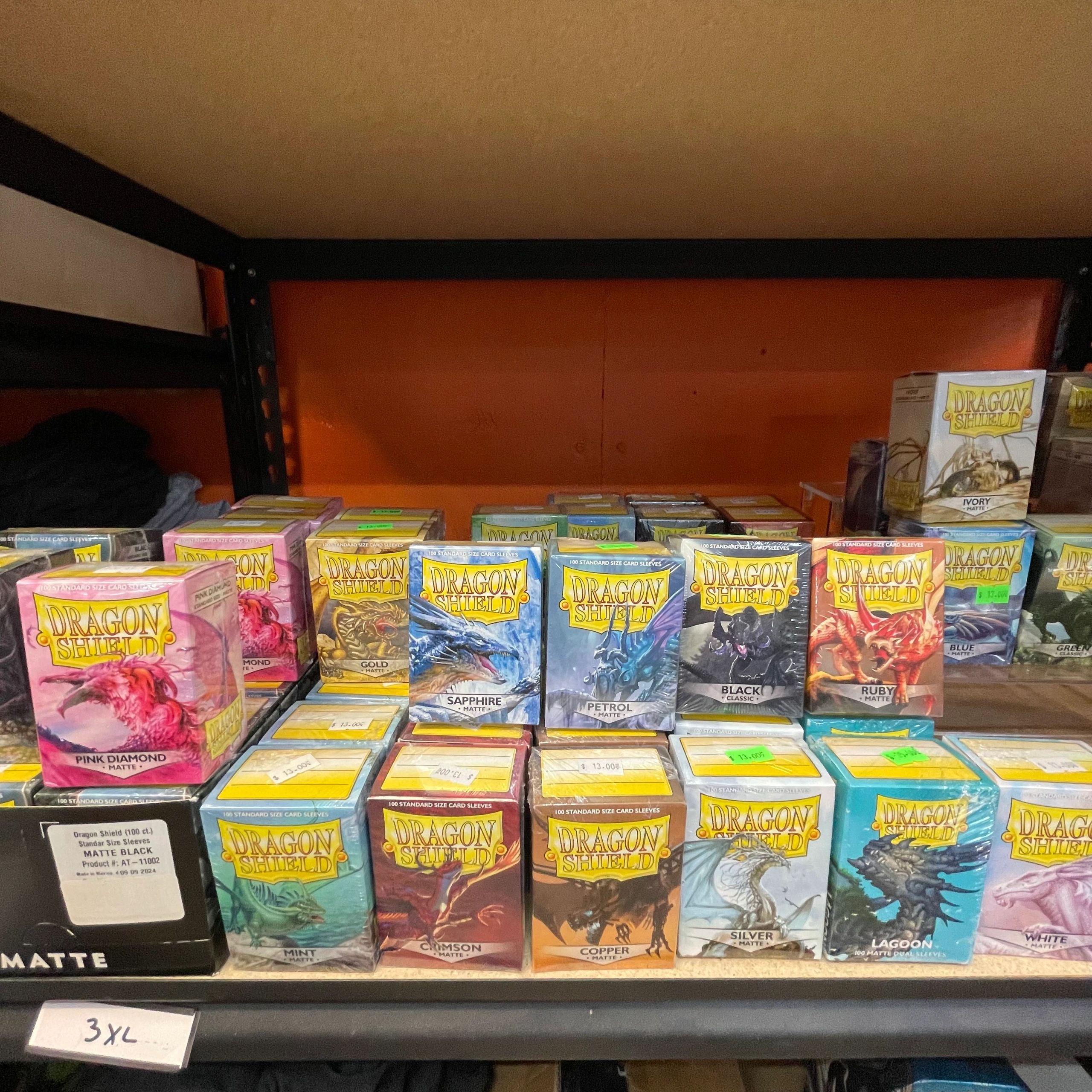 Various colorful Dragon Shield card sleeves displayed on a shelf.